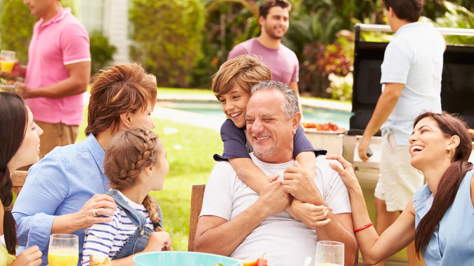 A multi-generation family laughing over a meal at a garden table in summer.