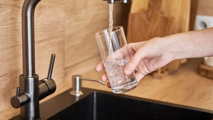 A hand filling a glass of water at a kitchen faucet.