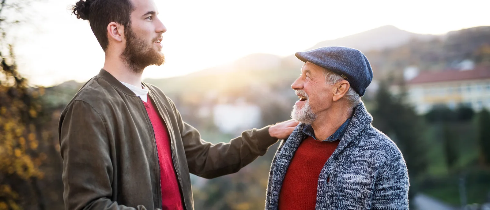 A father and his grown son laughing together on a walk through the countryside.
