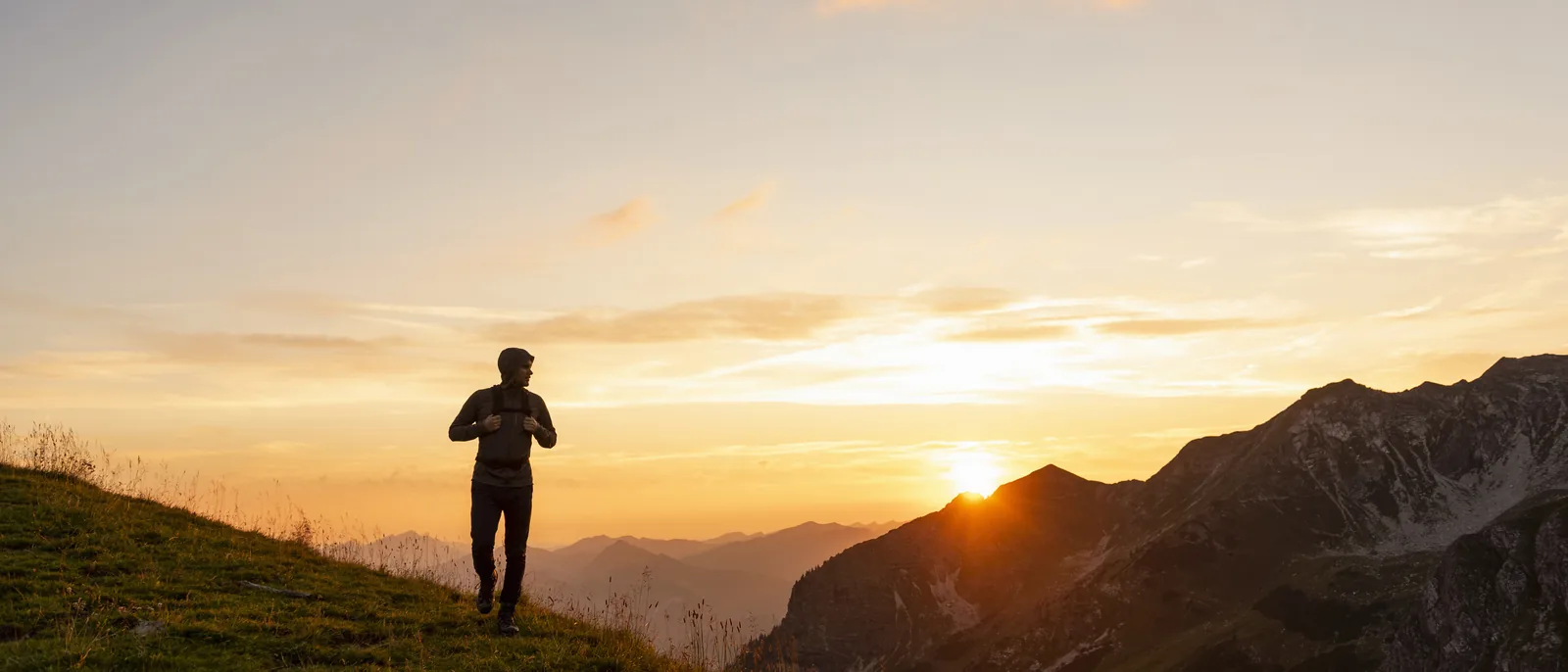 A lone hiker on a ridge at sunset, mountains behind.